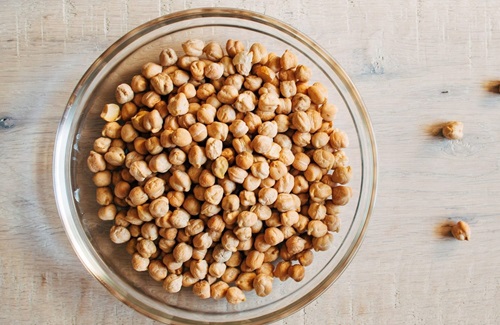 Garbanzos Primer plano de garbanzos cocidos y firmes en una cuchara de madera, listos para ser guisados.