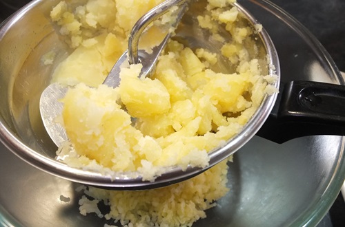 Moliendo papas para puré Moliendo papas cocidas con un prensador manual para obtener un puré suave.