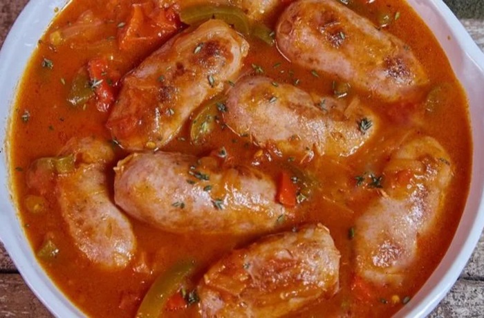 Chorizo a la pomarola: Receta tradicional argentina paso a paso Cazuela de barro con chorizos a la pomarola en salsa roja espesa con tiras de pimiento morrón.