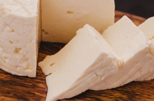 Queso semiduro Un bloque de queso de color amarillento con pequeños ojos, listo para ser rallado e integrado en la masa.