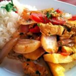 Lomo saltado de pollo con cebolla y tomate en sartén receta peruana